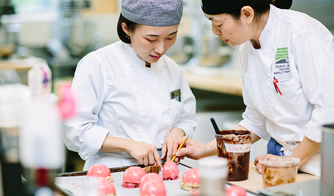 A VCC baking instructor and student look over pink pastries